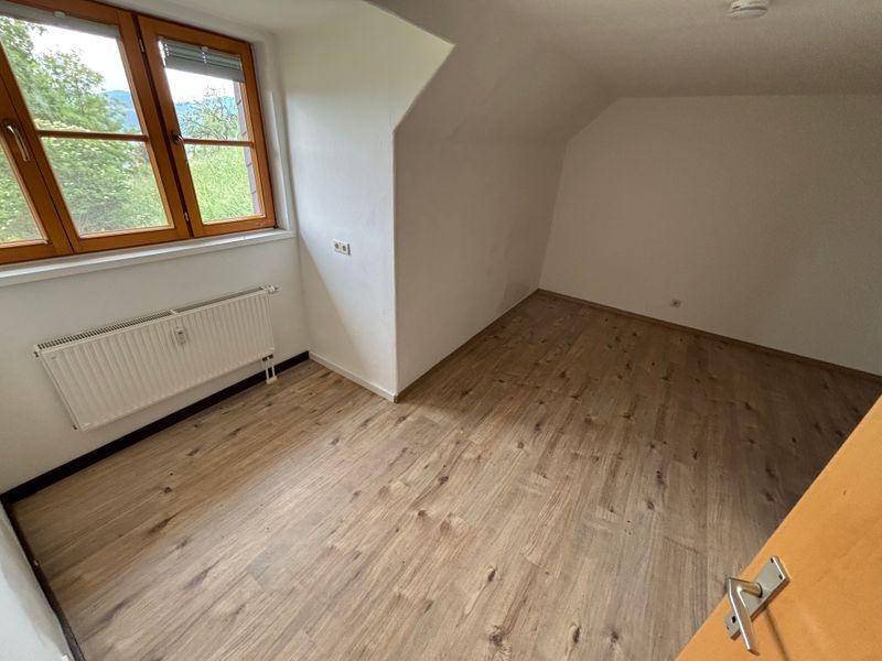 Geräumiges Zimmer im Dachgeschoss mit Holzboden, Schrägdecke und Fenster mit Ausblick.