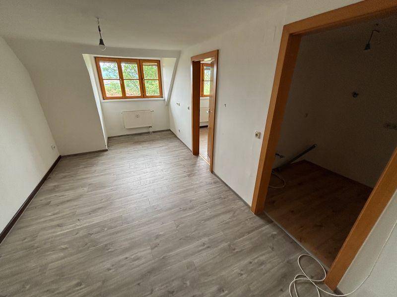 Helles Zimmer im Dachgeschoss mit Schrägdecke, Laminatboden und großem Fenster.