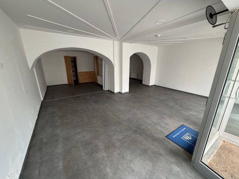 Geräumiger, leerer Geschäftsraum mit dunklem Boden, weißen Wänden und dekorativen Deckenbögen.