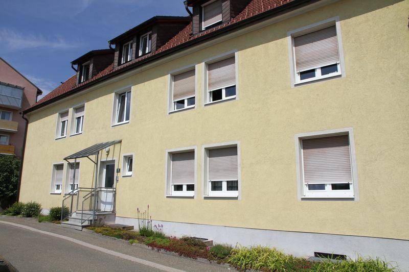Nahaufnahme der gelben Gebäudefassade mit Fenstern und geschlossenen Rollläden im Sonnenlicht.