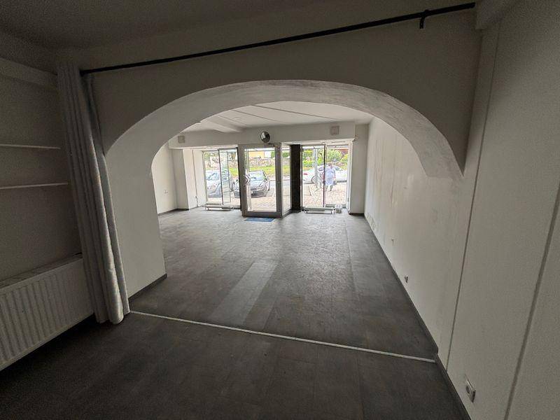 Blick durch einen Bogen auf den Eingangsbereich eines Geschäftsraums mit großen Fenstern zur Straße.