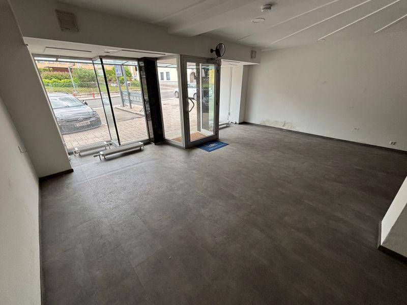 Heller Eingangsbereich eines Geschäftsraums mit großen Glasfronten zur Straße und dunklem Boden.