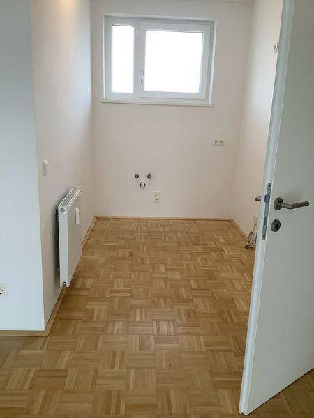 Leerer Raum mit Parkettboden, Fenster und Heizkörper, vorbereitet für Installationen.