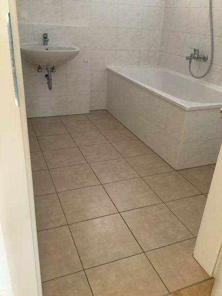 Helles Badezimmer mit Badewanne, Waschbecken und beigefarbenen Fliesen.