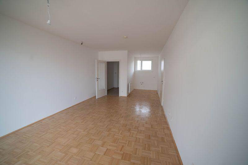 Geräumiger, leerer Wohnbereich mit Parkettboden und viel Tageslicht durch das Fenster.