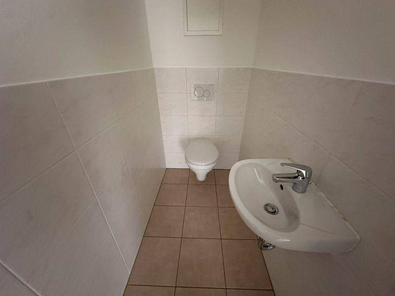 Kleines Gäste-WC mit Wand-WC, Waschbecken und hellbraunen Fliesen.