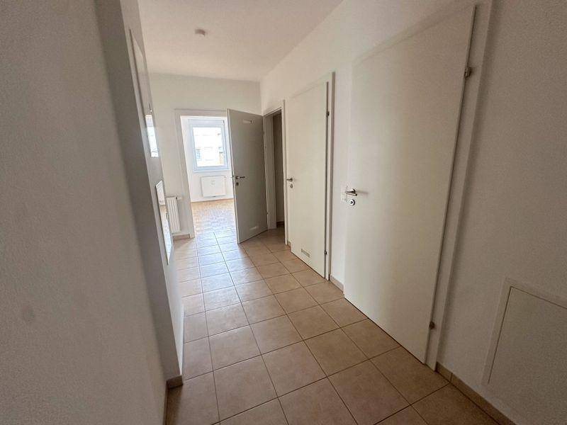Heller Flur mit Fliesenboden und Zugang zu verschiedenen Räumen, inklusive Blick in ein Zimmer.