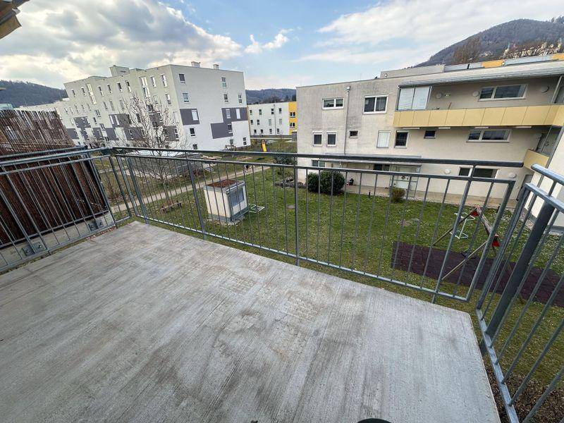 Betonbalkon mit Metallgeländer und Blick auf die umliegenden Gebäude und einen Spielplatz.