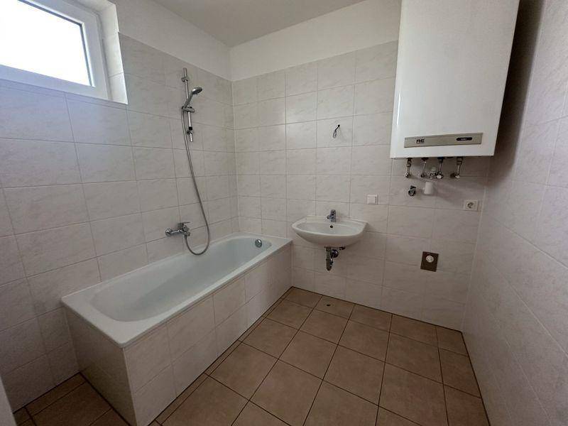 Badezimmer mit Badewanne, Waschbecken, Fenster und Wandfliesen in hellem Design.