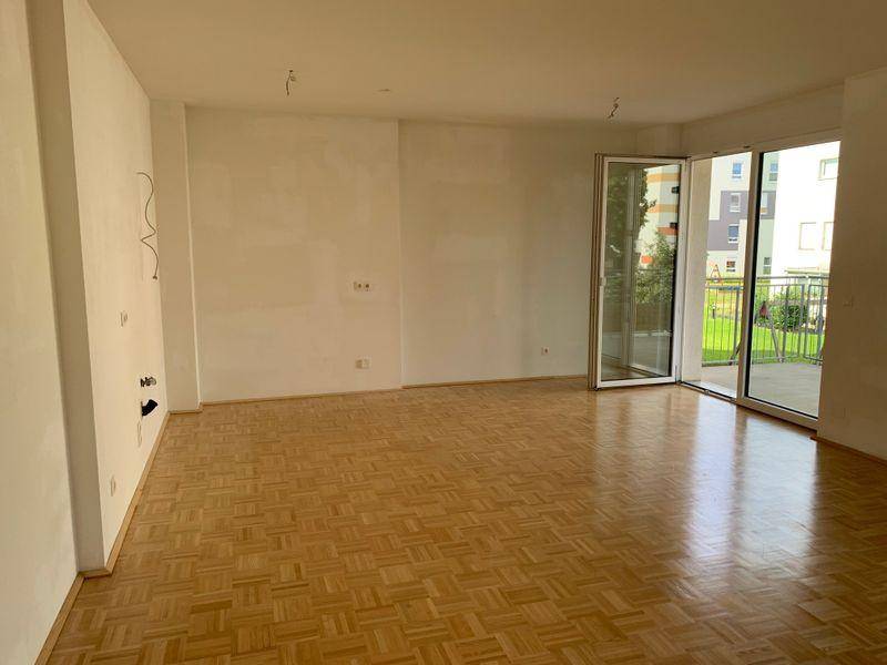 Geräumiges Wohnzimmer mit Parkettboden und großen Glasfenstern, die Zugang zum Außenbereich bieten.