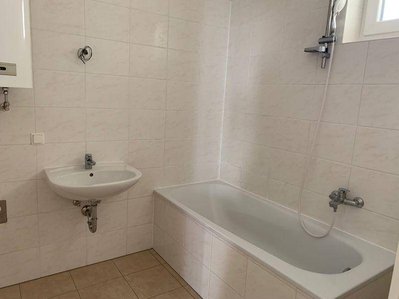 Badezimmer mit Badewanne, Waschbecken und hellen Wandfliesen, inklusive Fenster für Tageslicht.