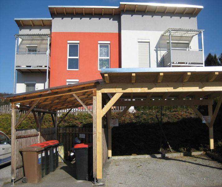 Modernes Gebäude mit Carport und Mülltonnen im Außenbereich unter strahlendem Sonnenschein.