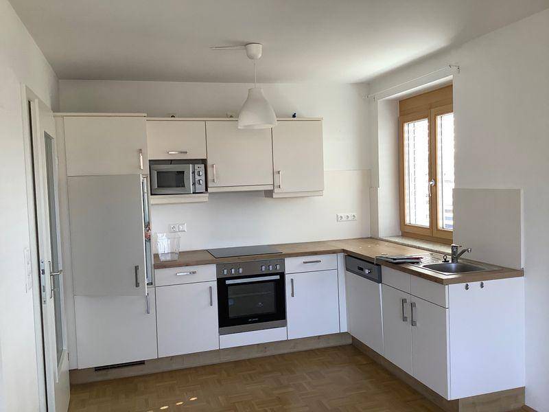 Funktionale Einbauküche mit weißen Schränken, Holz-Arbeitsplatte und integrierten Geräten.