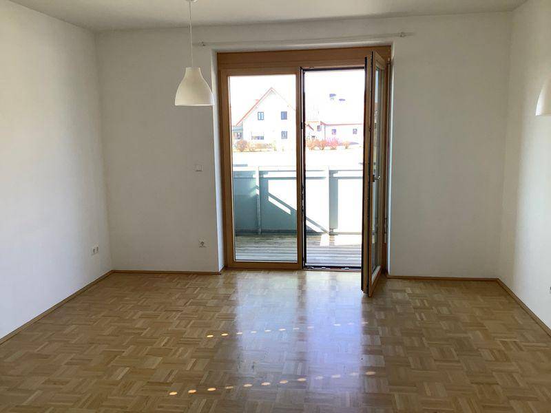 Heller Wohnraum mit Parkettboden und Zugang zu einem Balkon, ideal für natürliche Belichtung.