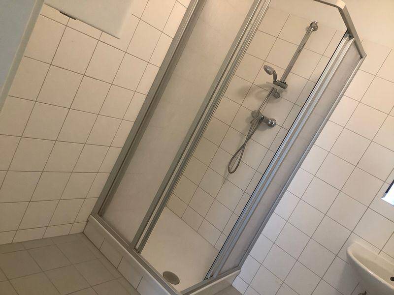 Helles Badezimmer mit weiß gefliesten Wänden und einer Duschkabine.