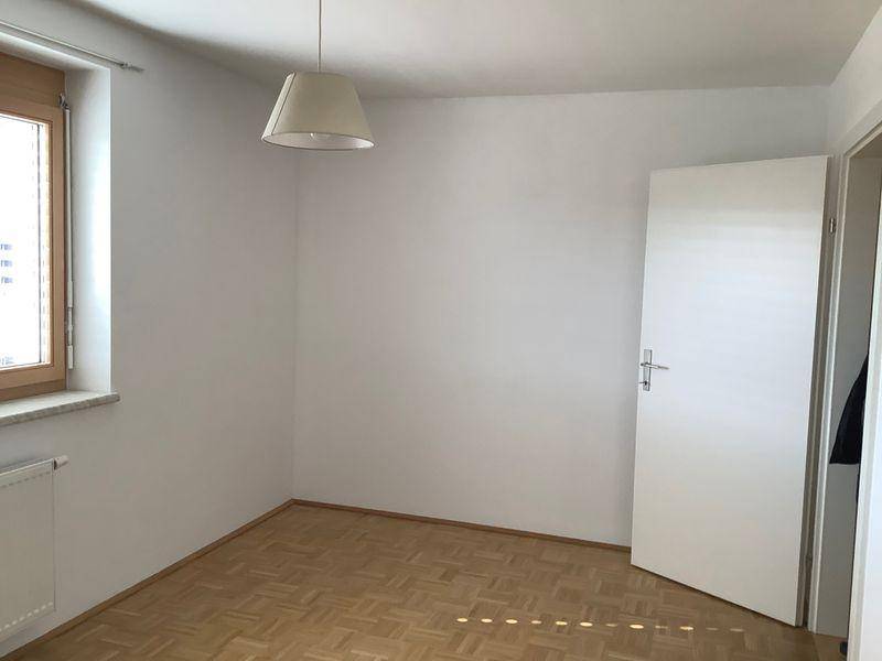 Leeres Schlafzimmer mit Parkettboden und einem Fenster, das viel Tageslicht hereinlässt.