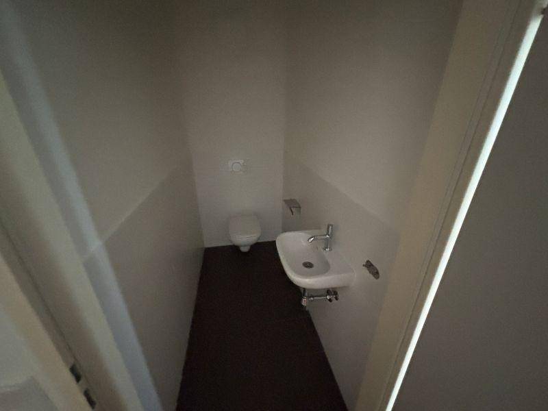 Kleines Gäste-WC mit Wand-WC und Waschbecken, ausgestattet mit dunklen Fliesen.