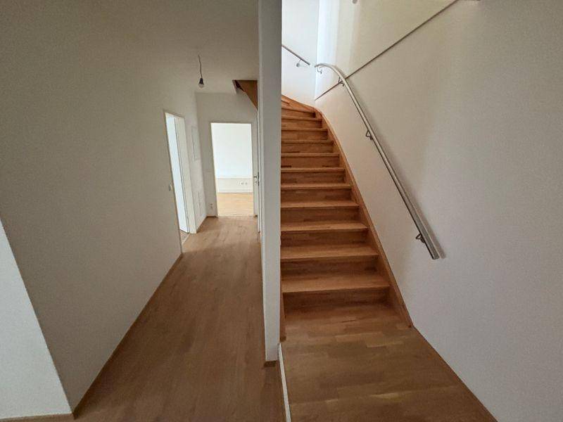 Geräumiger Flur mit Holztreppe und Metallgeländer, der die Etagen miteinander verbindet.