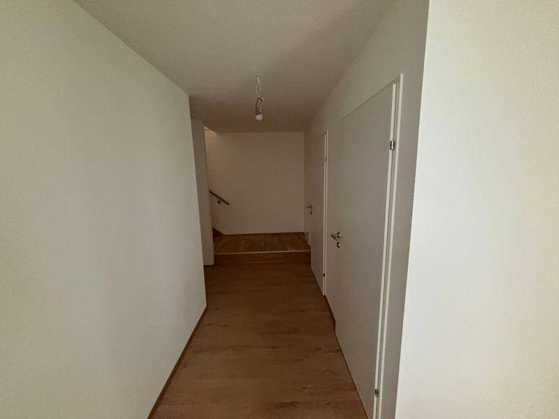 Heller Flur mit Holzfußboden und weißen Wänden, der zu weiteren Räumen führt.