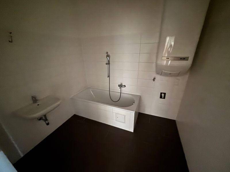 Badezimmer mit Badewanne, Waschbecken und Boiler, ausgestattet mit weißen Wandfliesen.