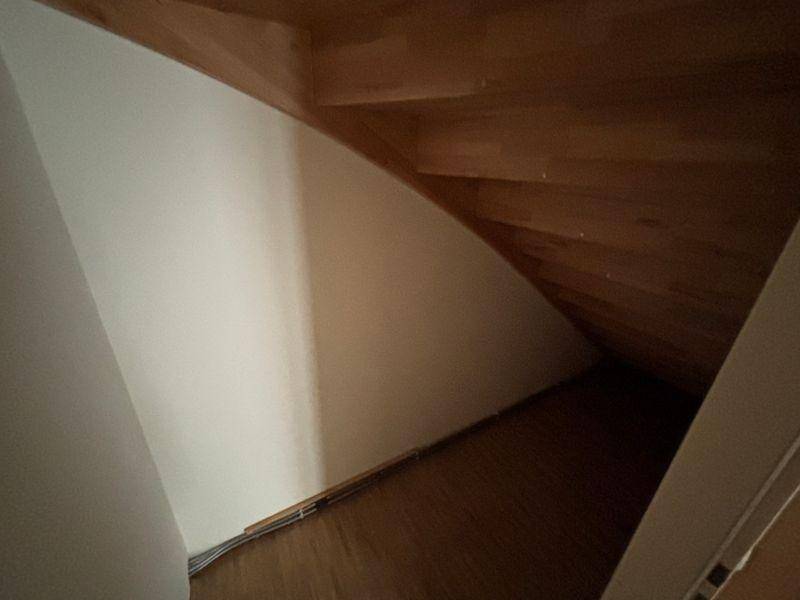 Bereich unter der Treppe mit Holzstufen und weißer Wand, als Stauraum nutzbar.