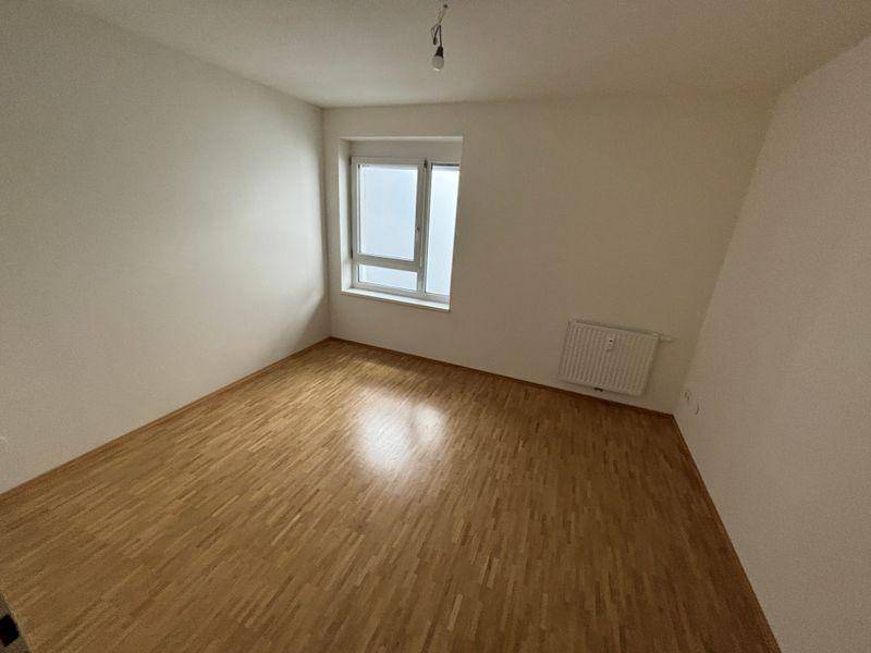 Helles Schlafzimmer mit Holzfußboden, weiß gestrichenen Wänden und Fenster.