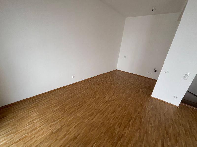 Geräumiger Wohnraum mit Holzfußboden und weißen Wänden, ideal für individuelle Gestaltung.