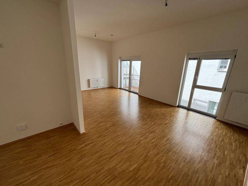 Lichtdurchfluteter Wohnbereich mit Holzfußboden und Zugang zu einem Balkon.