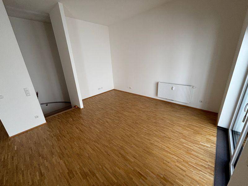 Heller Wohnbereich mit Holzfußboden, weißen Wänden und Heizkörper, bereit zur Einrichtung.