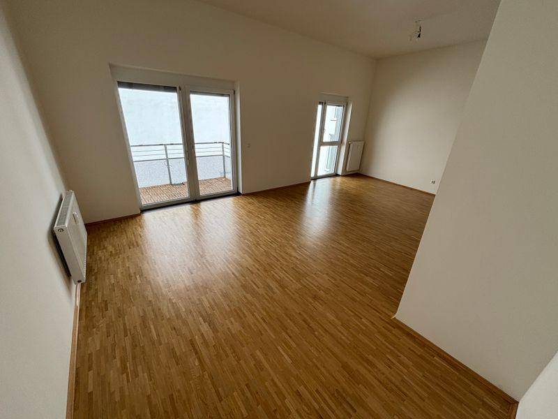 Großes Wohnzimmer mit Holzfußboden, Dachschrägen und Zugang zu zwei Balkonen.