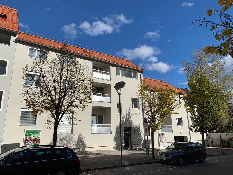 Mehrfamilienhaus mit weißer Fassade, roten Dächern und Balkonen unter blauem Himmel.
