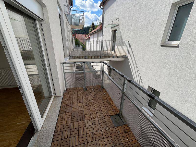 Balkon mit Holzdielenboden und Metallgeländer, bietet Platz für Sitzgelegenheiten.