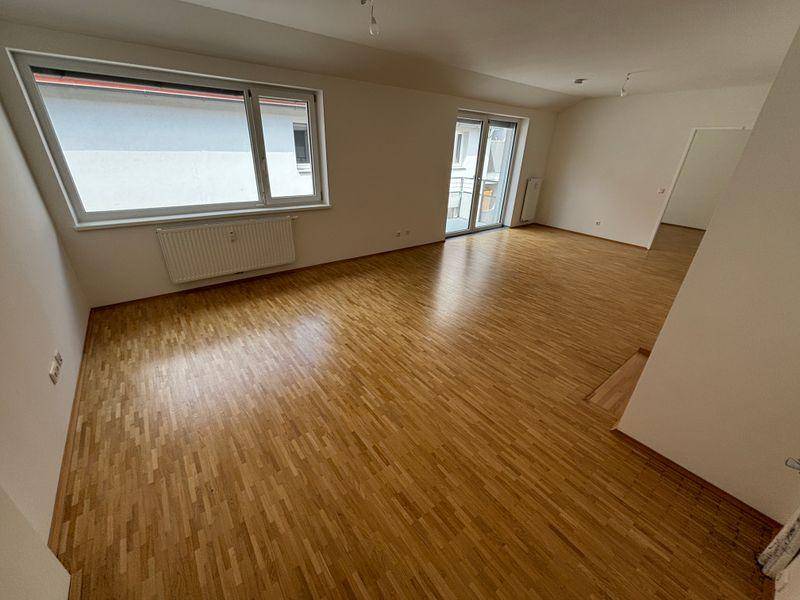Heller Wohnraum mit Parkettboden, großen Fenstern und Zugang zu einem Balkon.
