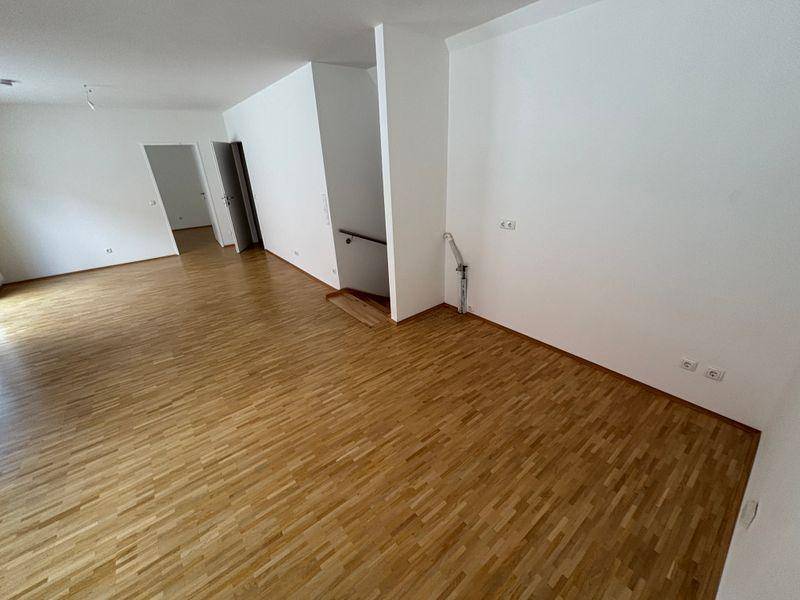 Geräumiger, heller Wohnbereich mit Parkettboden und weißen Wänden, bereit zur Einrichtung.