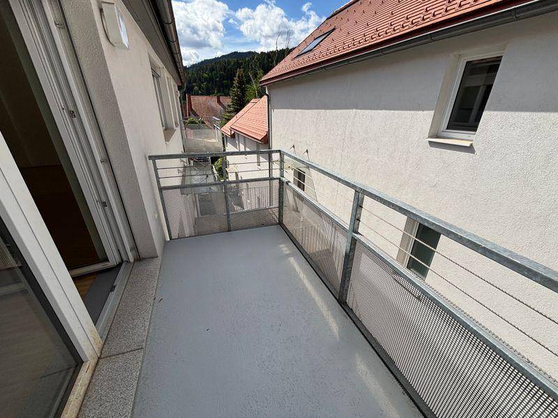 Balkon mit Metallgeländer und Blick auf die umliegenden Gebäude und grüne Hügel.