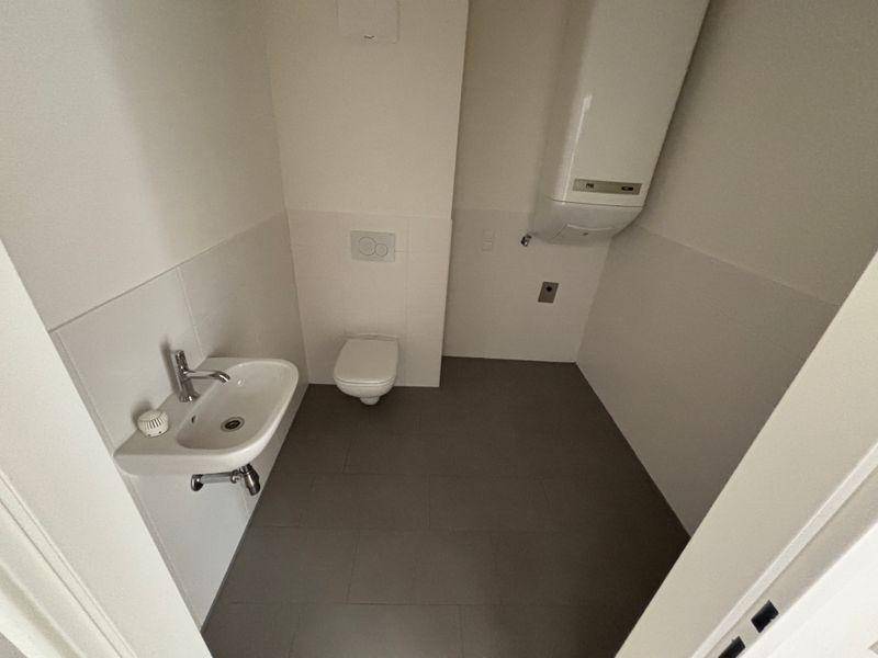 Modernes Gäste-WC mit Wand-WC, Waschbecken und Heizungsanlage an der Wand.