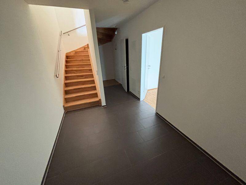 Heller Flur mit dunklen Fliesen und einer Holztreppe, die in die oberen Stockwerke führt.