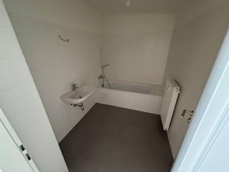 Helles Badezimmer mit Badewanne, Waschbecken und Heizkörper, bereit zur Nutzung.
