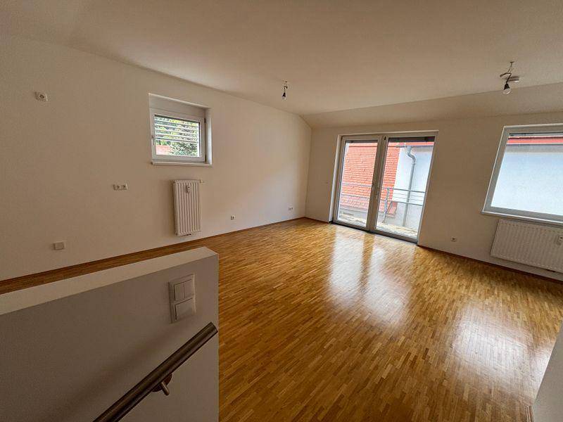 Geräumiges Wohnzimmer mit glänzendem Parkettboden und Zugang zu einem Balkon.