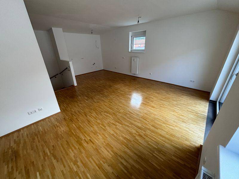 Heller Wohnbereich mit Parkettboden und weißen Wänden, bereit für individuelle Gestaltung.