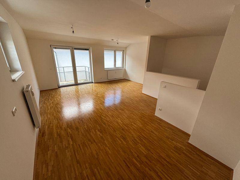 Lichtdurchfluteter Wohnraum mit Parkettboden und großen Fenstern, die auf einen Balkon führen.