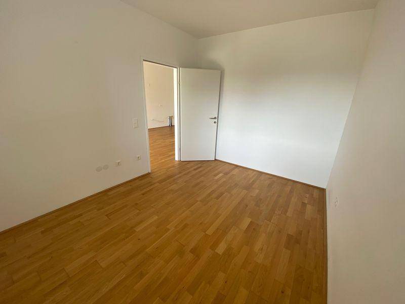 Leeres Zimmer mit hellem Holzboden und weißen Wänden, bereit zur individuellen Gestaltung.