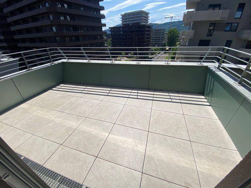 Geräumige, geflieste Terrasse mit Metallgeländer und urbanem Ausblick auf umliegende Gebäude.