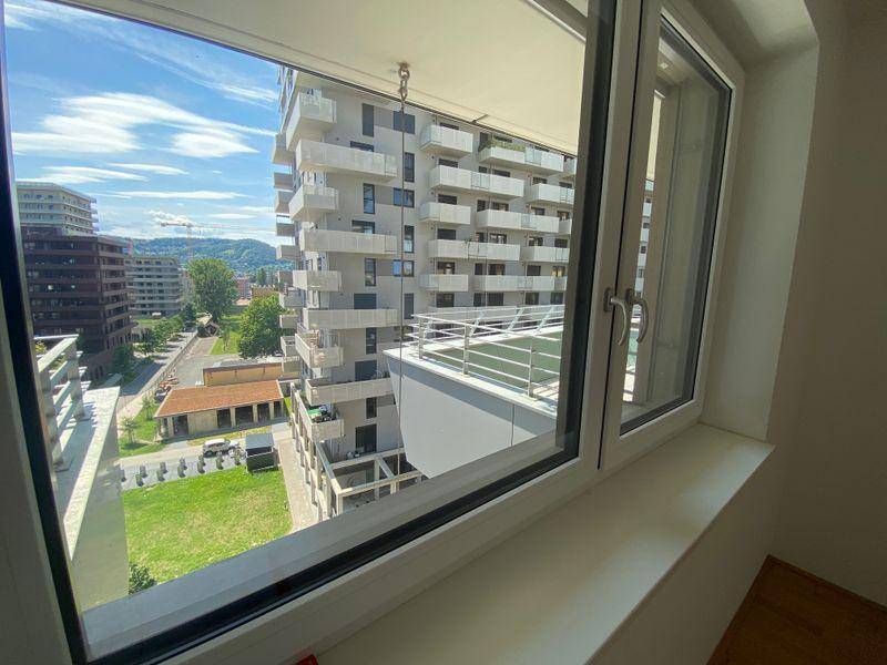 Blick aus einem Fenster auf ein gegenüberliegendes modernes Gebäude mit zahlreichen Balkonen.