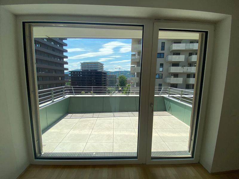 Große Glastüren öffnen sich zu einer geräumigen, gefliesten Terrasse mit Blick auf die Stadt.