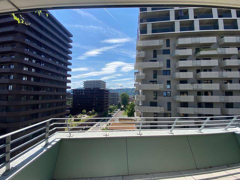 Sonniger Terrassenbereich mit Fliesenboden und weitem Blick über die Stadt und grüne Hügel.