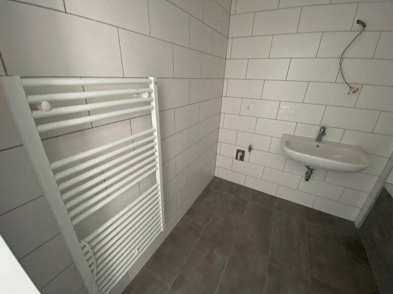 Helles Badezimmer mit beheiztem Handtuchhalter, Waschbecken und weißen Wandfliesen.