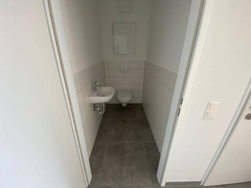 Kompaktes Gäste-WC mit Wand-WC, kleinem Waschbecken und hellen Fliesen an Wänden und Boden.