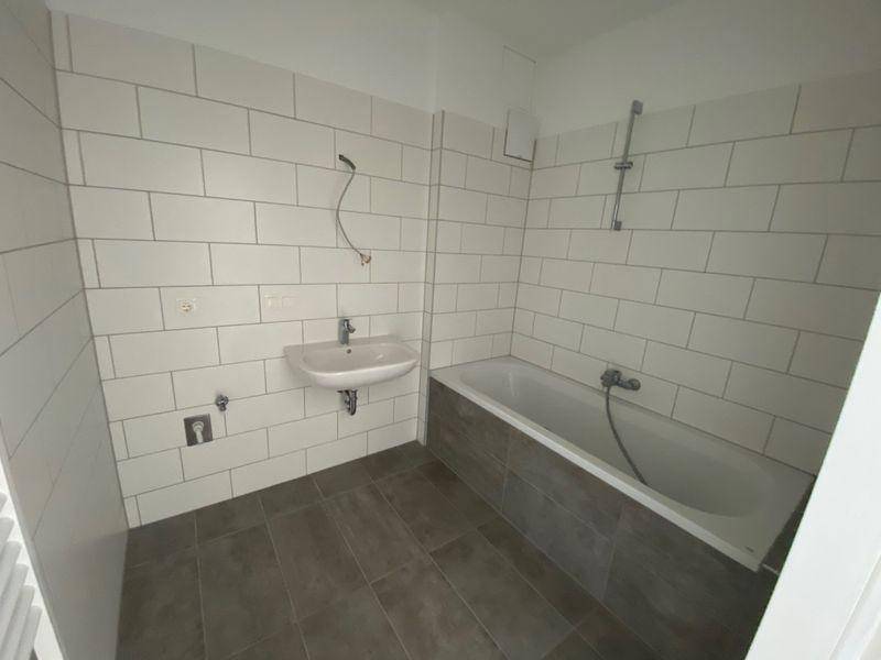 Modernes Badezimmer mit Badewanne, Waschbecken und weißen Wandfliesen sowie dunklem Fliesenboden.
