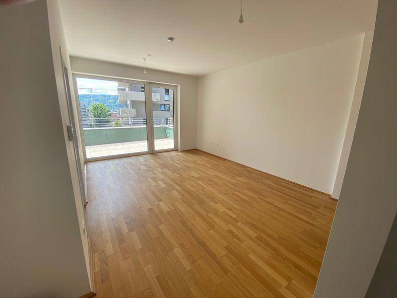 Geräumiges Wohnzimmer mit hellem Holzboden und großen Glastüren, die zur Terrasse führen.